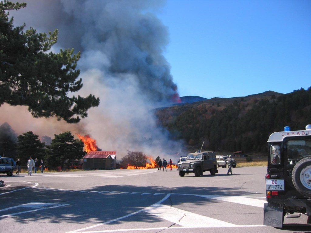 Figura 7 - Le colate laviche invadono il piazzale della stazione turistica Etna Nord, incendiando la vegetazione e le strutture ricettive realizzate in legno.