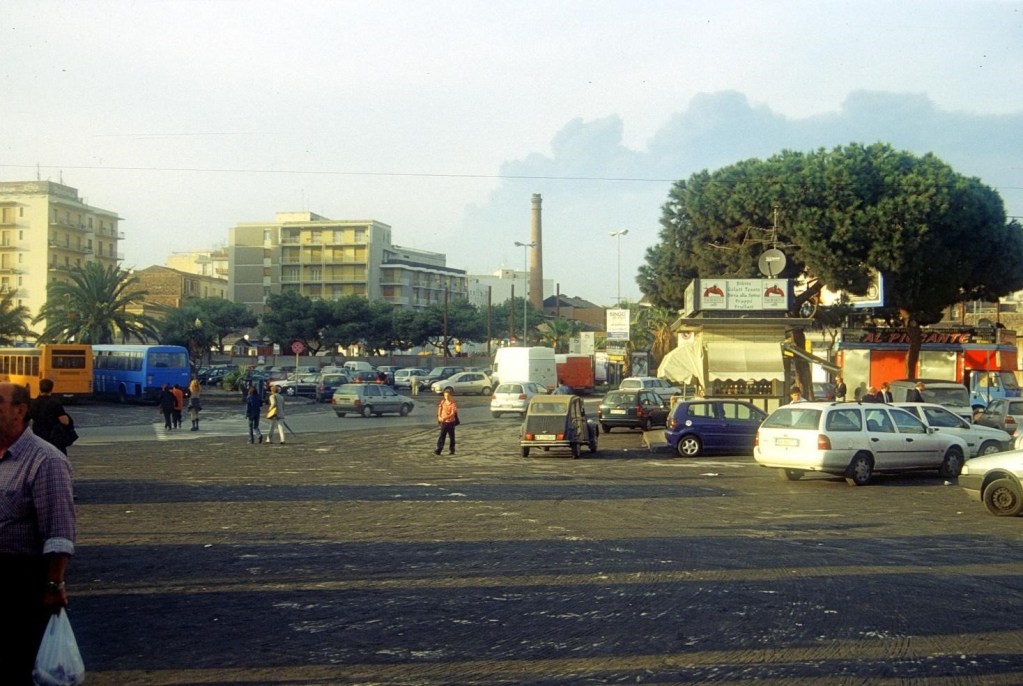 Figura 8 - La piazza antistante la Stazione Centrale di Catania sotto la cenere, 2 novembre 2002. Sullo sfondo si vede la nube eruttiva, che continua ad essere emessa dalle bocche sull’alto fianco meridionale dell’Etna.
