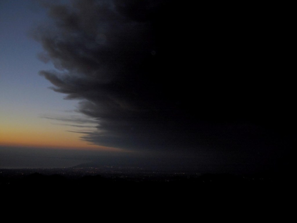 Figura 1 - Una densa nube eruttiva oscura il cielo alle prime luci dell’alba del 27 ottobre 2002. La nube eruttiva è prodotta da una bocca eruttiva apertasi nella tarda serata del 25 ottobre sull’alto fianco meridionale dell’Etna. Sullo sfondo si intravedono il Golfo di Catania e la costa tra Brucoli e Augusta.