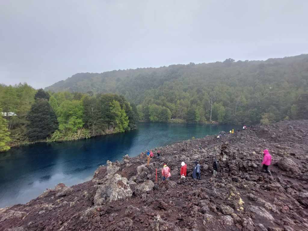 Figura 8 - Veduta del Lago Arcoiris, nel Geoparco di Kutralkura, Cile. Il lago si è formato circa 320 anni fa durante un’eruzione del vulcano Llaima,quando una colata di lava (in primo piano, quella su cui camminano le persone) ha sbarrato il corso di un fiume.